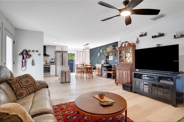 living room featuring visible vents, light wood-style flooring, and ceiling fan with notable chandelier