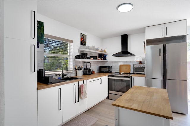 kitchen featuring butcher block countertops, appliances with stainless steel finishes, white cabinetry, wall chimney range hood, and backsplash