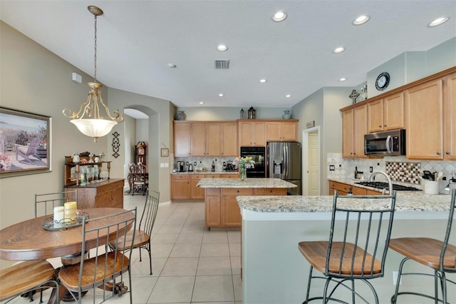 kitchen with a peninsula, light tile patterned flooring, arched walkways, appliances with stainless steel finishes, and a center island