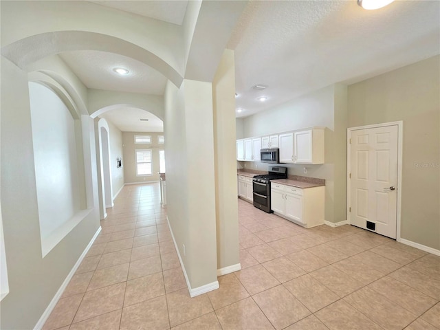 hall featuring arched walkways, light tile patterned floors, a textured ceiling, and baseboards