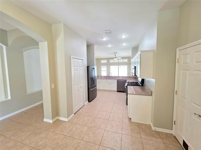 kitchen with baseboards, ceiling fan, light tile patterned floors, white cabinets, and stainless steel appliances