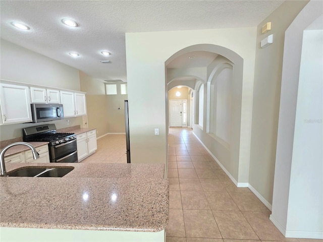 kitchen with light stone countertops, light tile patterned floors, stainless steel appliances, white cabinetry, and a sink