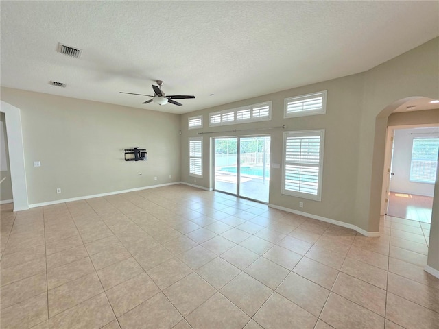 unfurnished room featuring a ceiling fan, a textured ceiling, arched walkways, light tile patterned floors, and baseboards