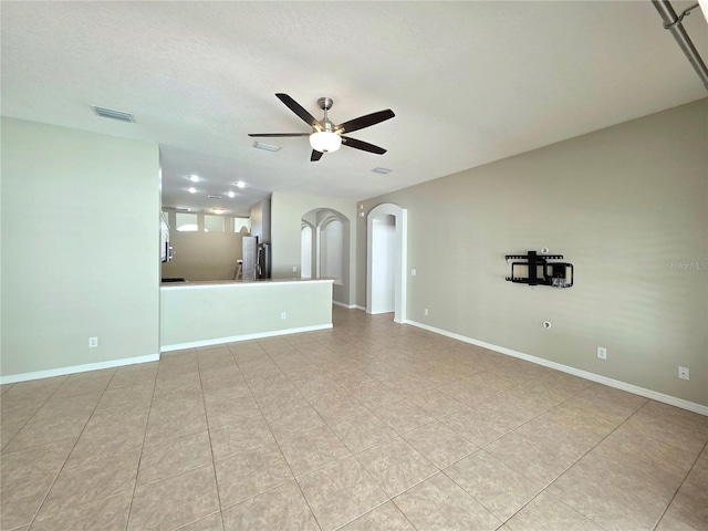 unfurnished living room featuring arched walkways, visible vents, baseboards, and a ceiling fan