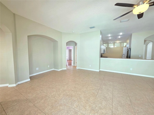 unfurnished living room with visible vents, a ceiling fan, arched walkways, and baseboards