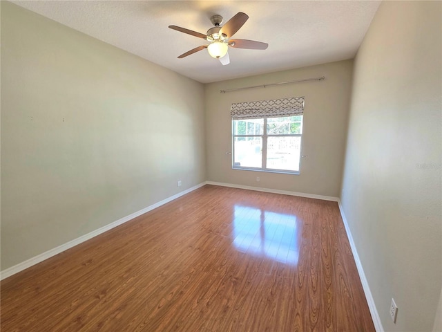 empty room featuring wood finished floors, baseboards, and ceiling fan