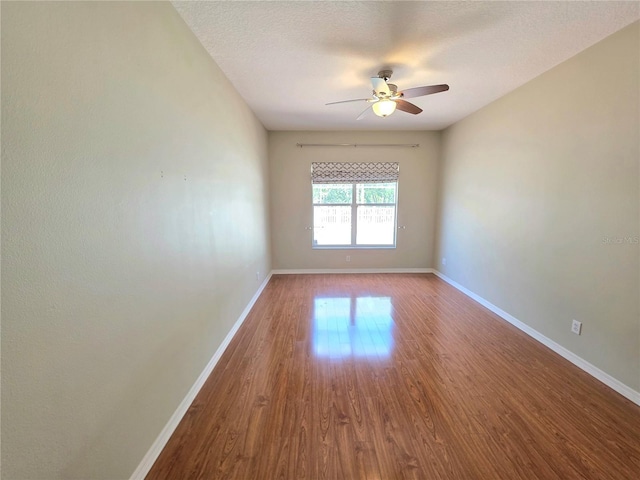 empty room with a textured ceiling, wood finished floors, baseboards, and ceiling fan