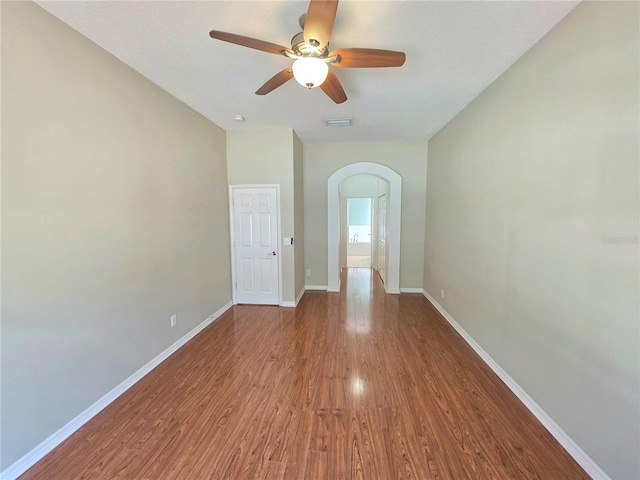 spare room featuring visible vents, baseboards, wood finished floors, arched walkways, and a ceiling fan