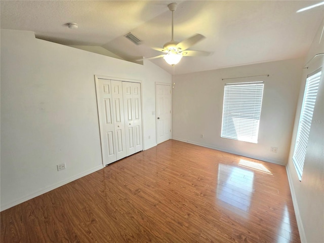 unfurnished bedroom featuring visible vents, baseboards, vaulted ceiling, wood finished floors, and a ceiling fan