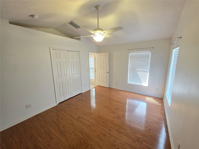 unfurnished bedroom with wood finished floors, visible vents, baseboards, vaulted ceiling, and a closet