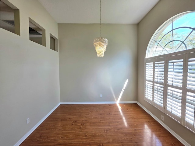 unfurnished dining area with baseboards, an inviting chandelier, and wood finished floors