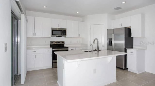 kitchen featuring an island with sink, a sink, light countertops, appliances with stainless steel finishes, and white cabinetry