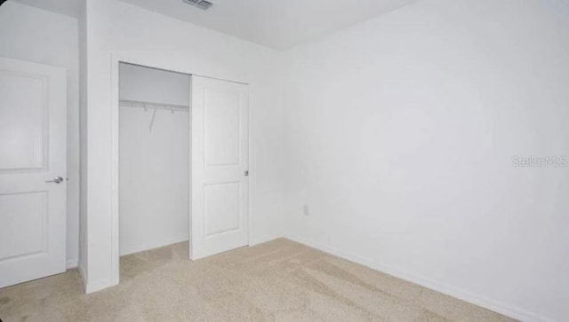 unfurnished bedroom featuring visible vents, a closet, and light carpet