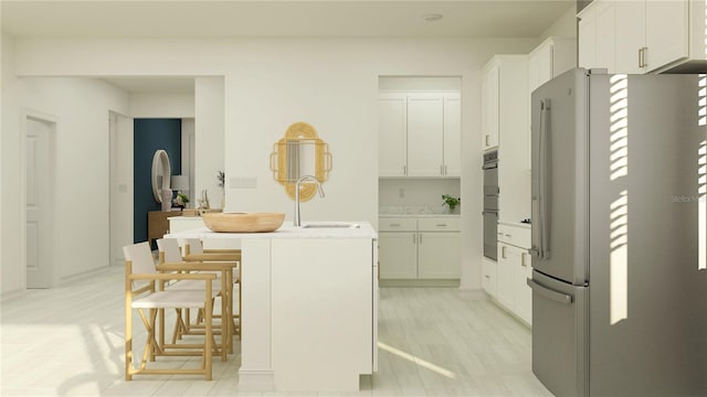 kitchen featuring a center island with sink, a sink, white cabinetry, freestanding refrigerator, and a breakfast bar area