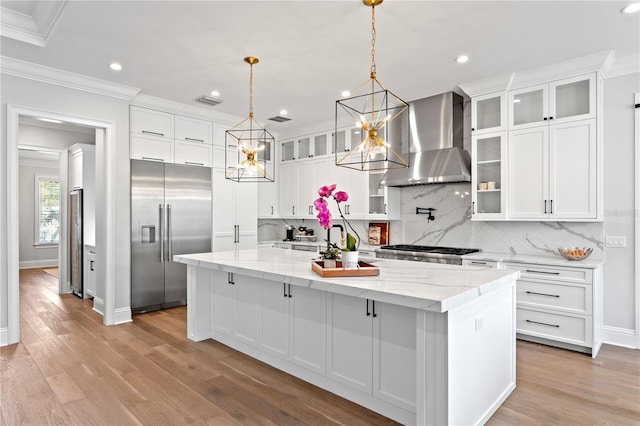 kitchen featuring stainless steel built in fridge, a spacious island, wall chimney exhaust hood, and white cabinetry