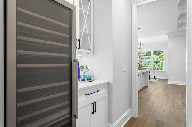 hallway with wood finished floors, baseboards, recessed lighting, ornamental molding, and wine cooler