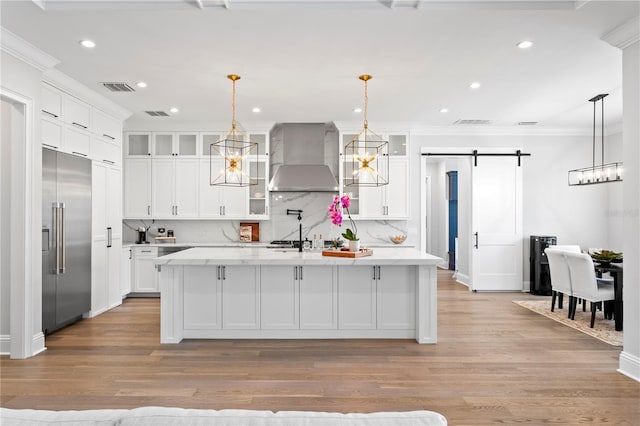 kitchen featuring white cabinetry, a barn door, wall chimney exhaust hood, and stainless steel built in refrigerator