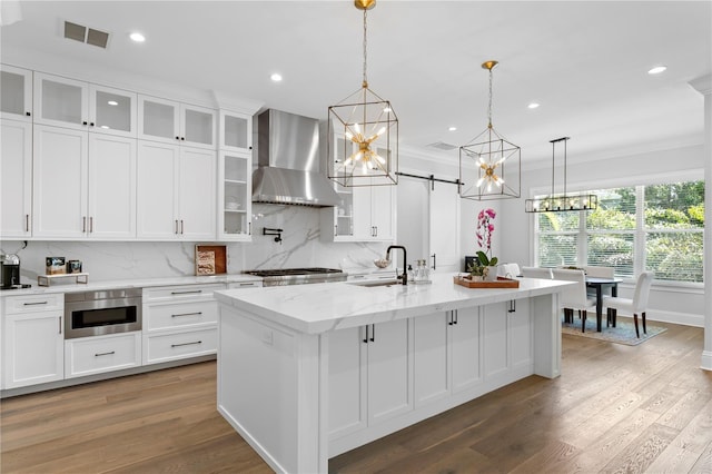 kitchen with visible vents, ornamental molding, a sink, a barn door, and wall chimney range hood