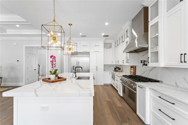 kitchen with a sink, crown molding, white cabinets, wall chimney exhaust hood, and a kitchen island with sink