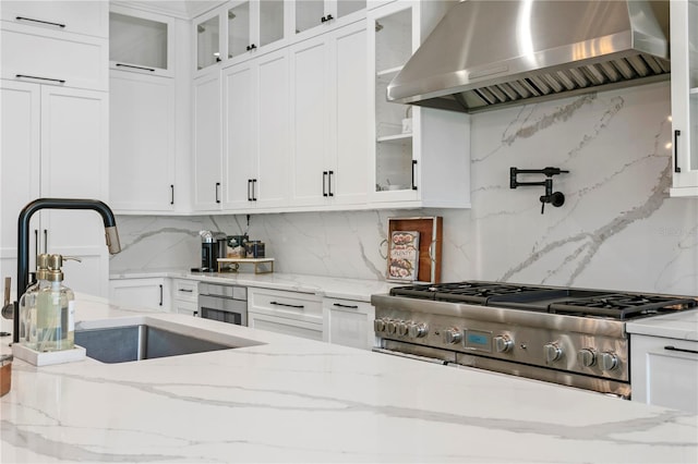 kitchen featuring a sink, light stone countertops, white cabinets, and wall chimney range hood