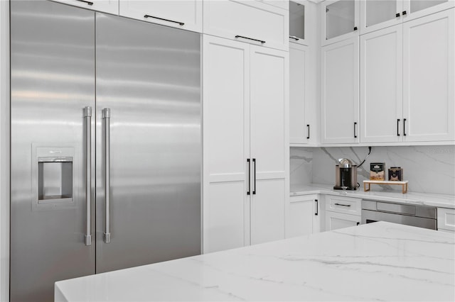 kitchen featuring light stone counters, built in fridge, and white cabinets