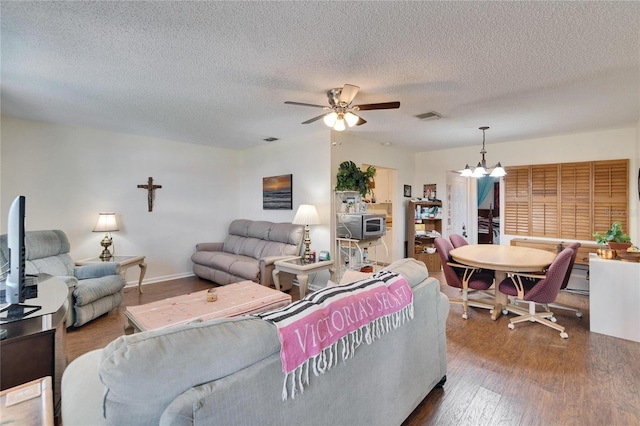 living area featuring visible vents, a textured ceiling, ceiling fan with notable chandelier, and wood finished floors