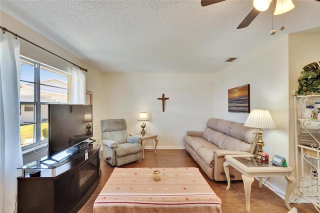 living area with visible vents, wood finished floors, baseboards, ceiling fan, and a textured ceiling
