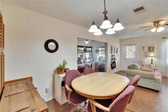 dining space featuring visible vents, wood finished floors, baseboards, a textured ceiling, and ceiling fan with notable chandelier