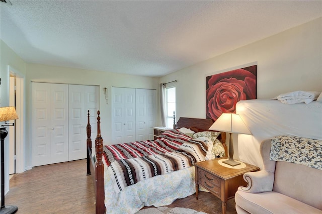bedroom featuring two closets, a textured ceiling, and wood finished floors