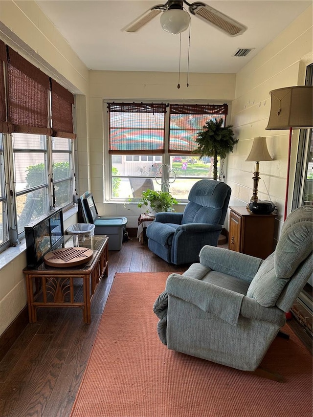 living area featuring concrete block wall, ceiling fan, hardwood / wood-style floors, and visible vents