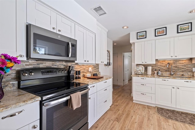 kitchen with visible vents, a sink, appliances with stainless steel finishes, white cabinets, and light wood finished floors