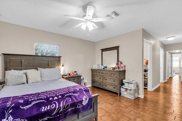 bedroom with visible vents, baseboards, ceiling fan, light wood-type flooring, and a textured ceiling