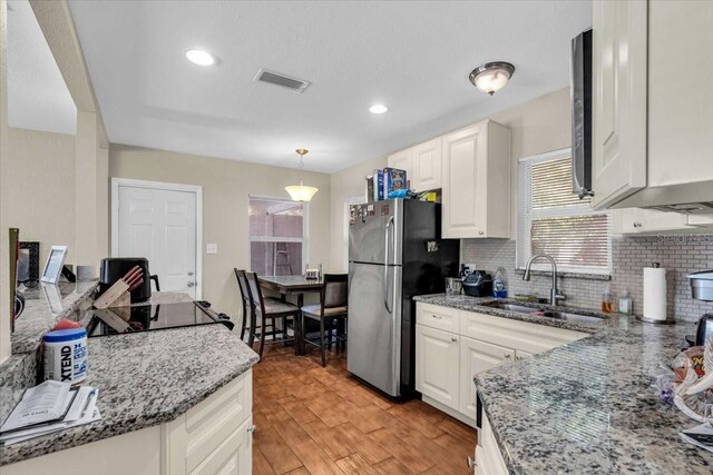kitchen with freestanding refrigerator, white cabinetry, a sink, light wood finished floors, and backsplash