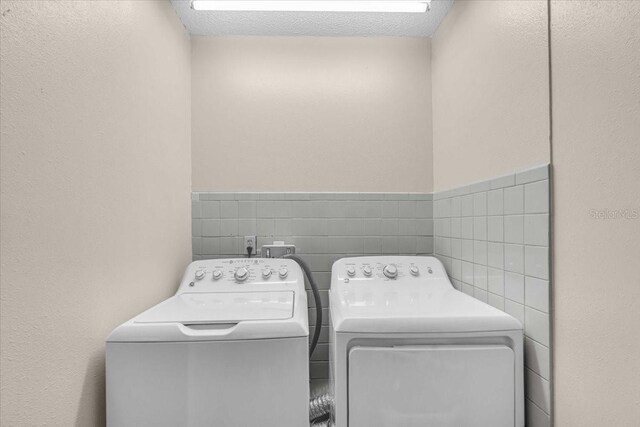 washroom featuring separate washer and dryer, laundry area, tile walls, and a textured wall