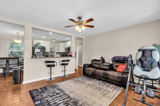 living area featuring a ceiling fan, baseboards, visible vents, and wood finished floors