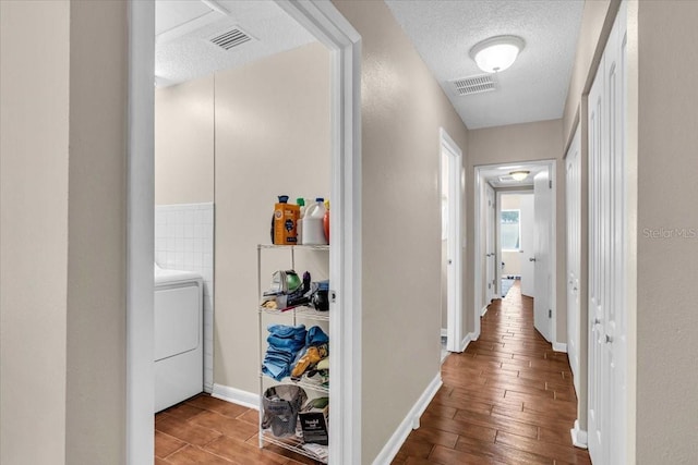 hall featuring washer / clothes dryer, a textured ceiling, visible vents, and wood finished floors