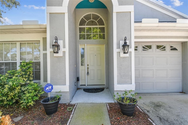 entrance to property featuring concrete driveway, a garage, and stucco siding