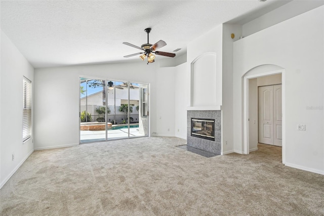 unfurnished living room featuring baseboards, carpet, a tiled fireplace, a textured ceiling, and a ceiling fan