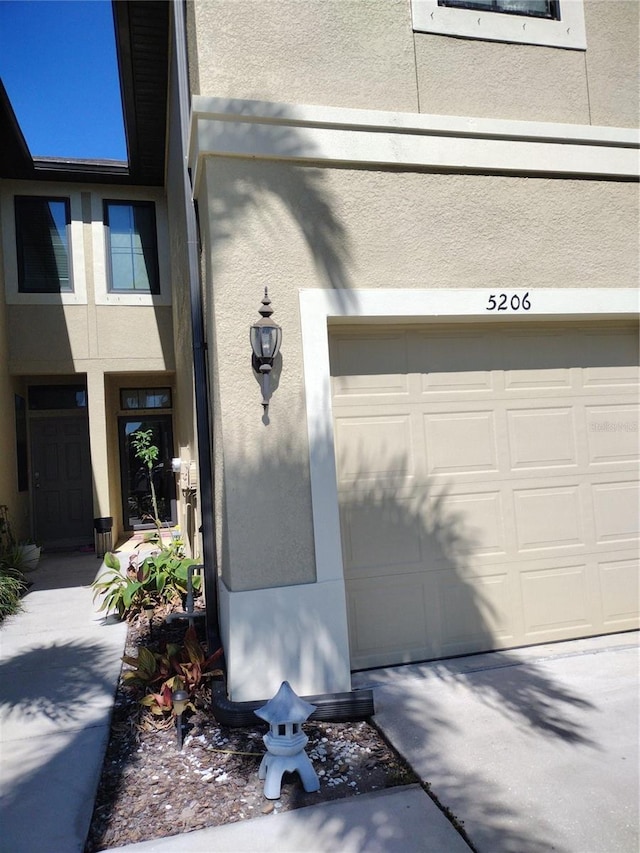 view of exterior entry with an attached garage, driveway, and stucco siding