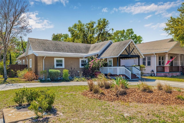 view of front facade featuring a front lawn, fence, covered porch, stucco siding, and driveway