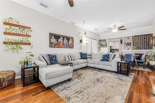 living room with visible vents, wood finished floors, ceiling fan, and crown molding