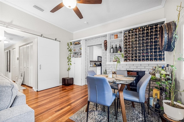 dining space with visible vents, crown molding, ceiling fan, a barn door, and wood finished floors