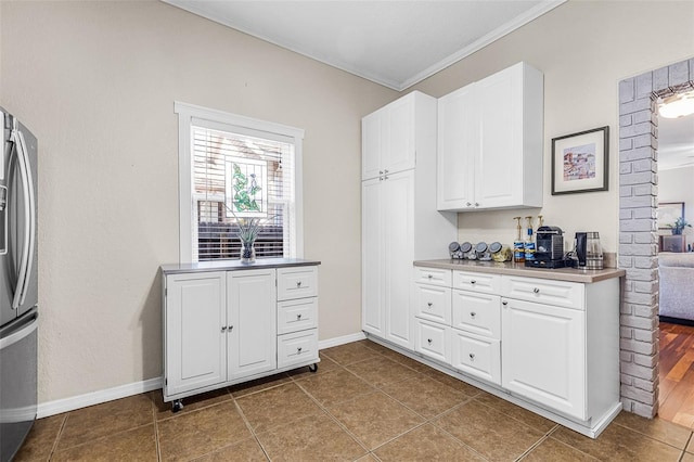 kitchen featuring white cabinets, stainless steel fridge with ice dispenser, baseboards, and ornamental molding