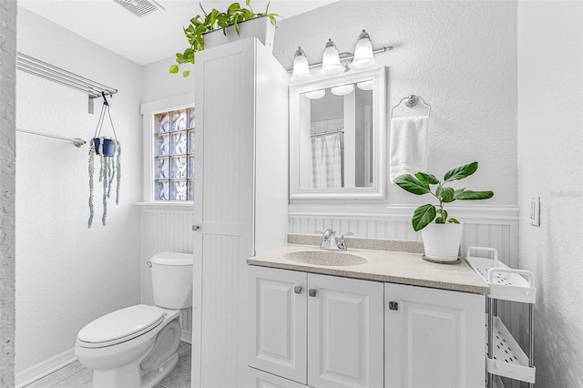 full bath featuring visible vents, toilet, vanity, and a textured wall