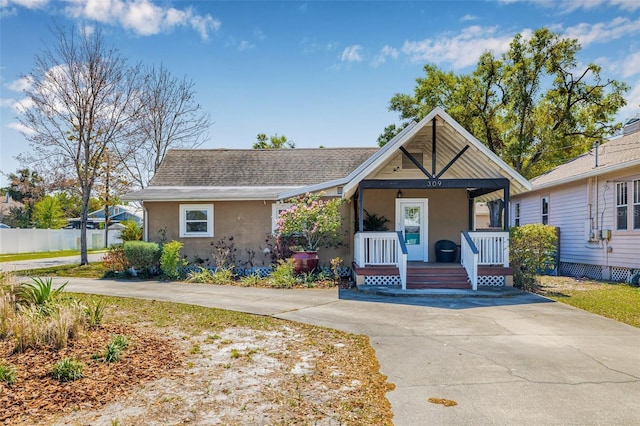 view of front of property with fence, driveway, roof with shingles, covered porch, and stucco siding