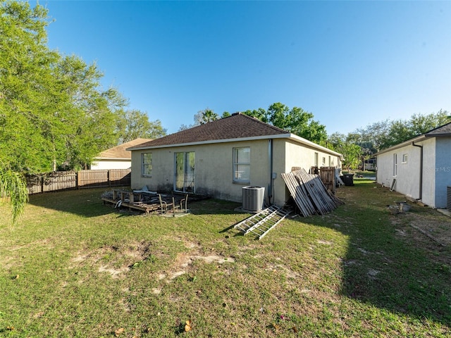 rear view of house featuring stucco siding, fence, a yard, a shingled roof, and central AC unit