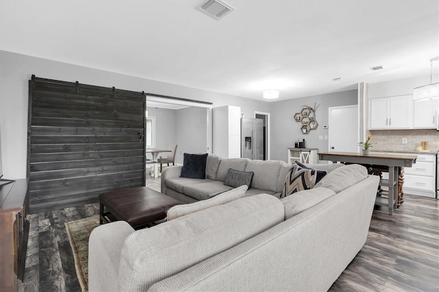 living area featuring a barn door, visible vents, and dark wood finished floors