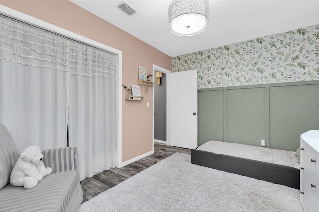 bedroom featuring wood finished floors, visible vents, wallpapered walls, wainscoting, and a decorative wall