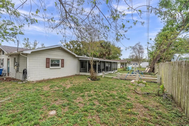 rear view of property featuring a lawn, concrete block siding, fence, and a sunroom