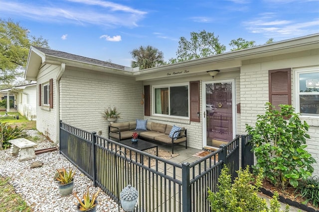 view of exterior entry featuring brick siding, outdoor lounge area, and fence